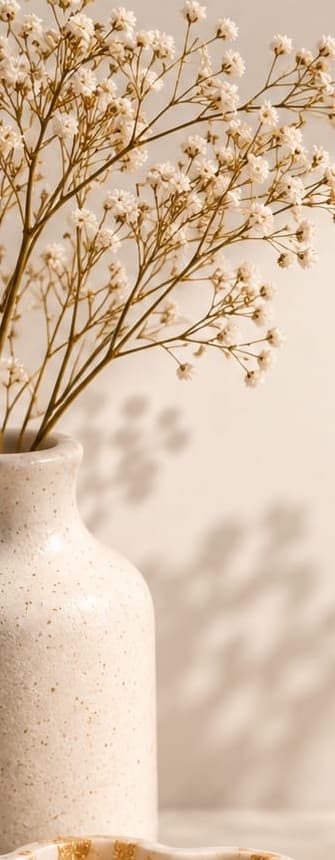 Speckled ceramic vase holding dried gypsophila in soft morning light
